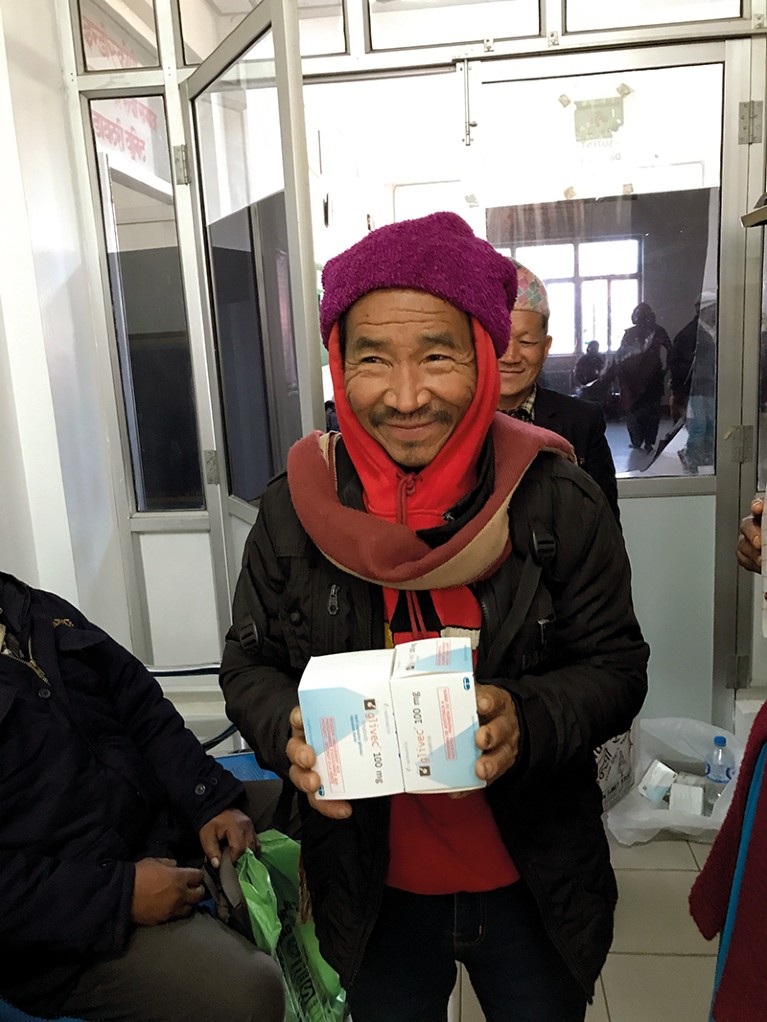 A smiling man holds up boxes containing cancer drugs.