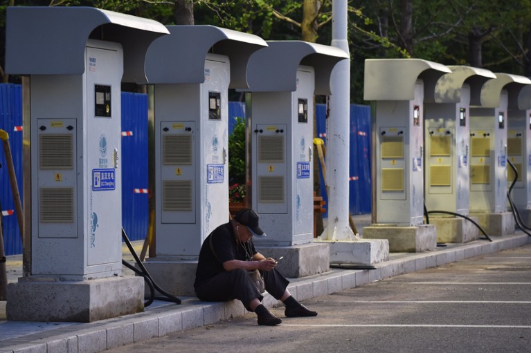 A man sits in front of unused electric car charging stations