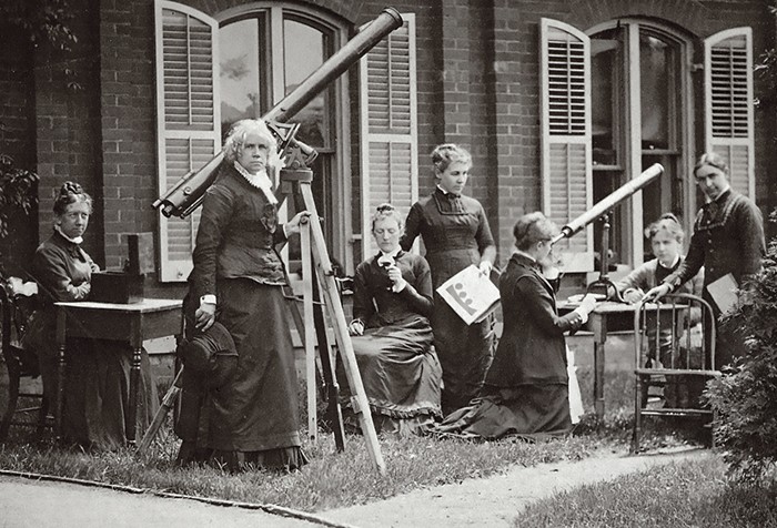 Photograph of Maria Mitchell and her students measuring the sun's rotation with small telescopes outside the old observatory.