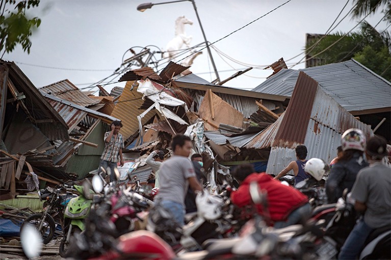Residents look for belongings amid debris in Palu in Sulawesi.In the background are collapsed houses, a lampost and horse statue