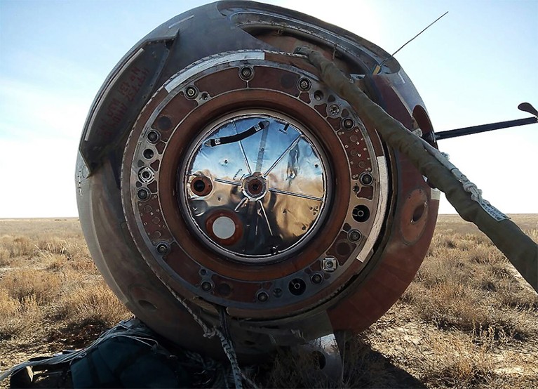A view of the round Soyuz MS-10 space capsule on a grassy plane