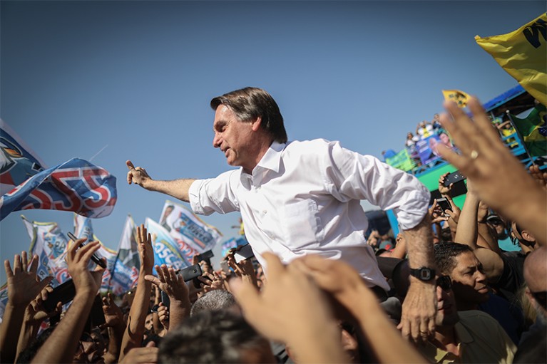 Jair Bolsonaro raises his fist into the air whilst surrounded by supporters during a campaign rally.