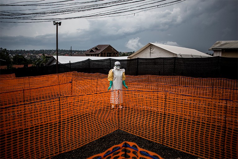 A health worker waits to handle a new unconfirmed ebola patient in a lane created with orange barrier tape.