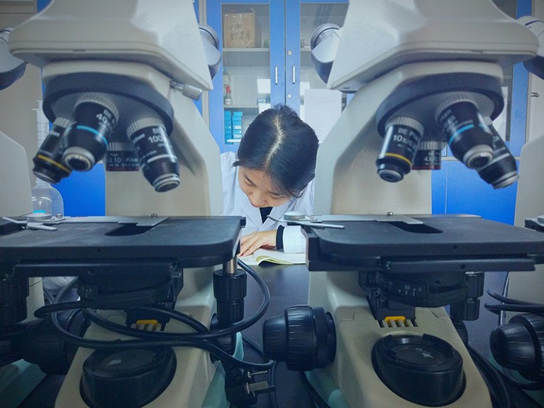 A researcher works at a desk between two microscopes