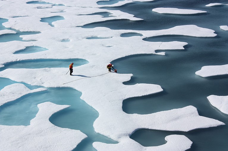 Two scientists measure ice in the arctic.
