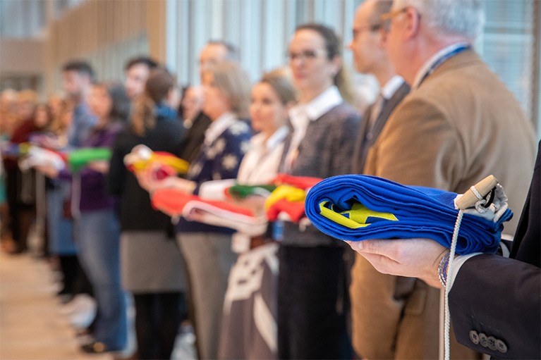 A row of EMA staff hold bundled flags from EU countries in their London office.