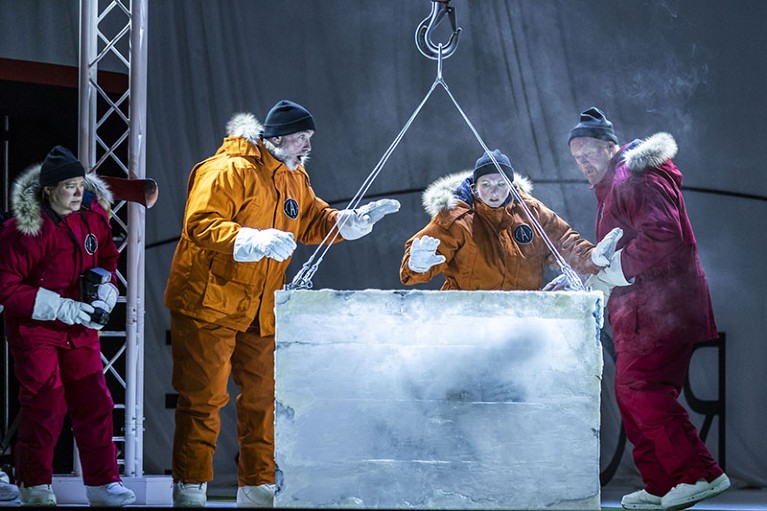 Four opera singers on stage, dressed in Arctic gear, crowd around a block of ice.