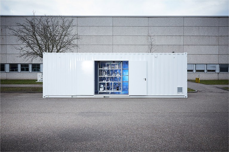 A chemical reactor sits inside a long, white rectangular shipping container.