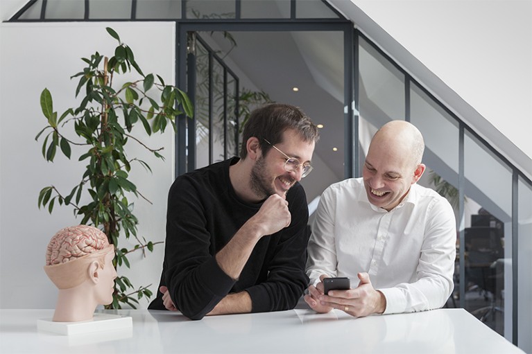Stefan Greiner and Markus Dahlem smile while looking at a mobile phone.