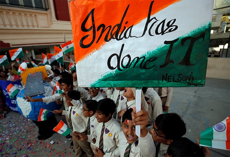 A boy holds up a sign saying 'India has done it' while his classmates celebrate in a school playground in Ahmedabad.