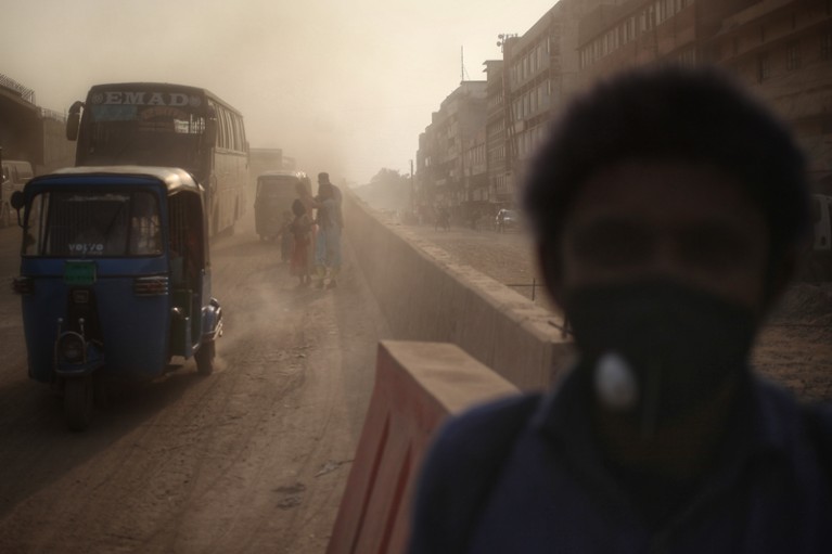 People walking through a dusty road with vehicles in Dhaka, Bangladesh