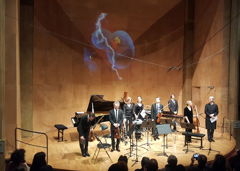 Seven musicians on a stage, with a scientific image projected onto the wall behind them.
