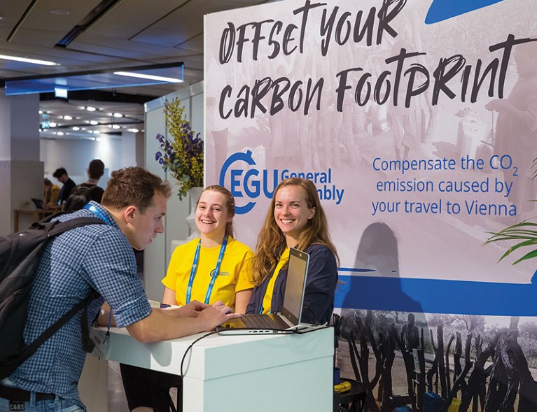 A conference attendee talks to some people on a stand promting how to offset your carbon footprint