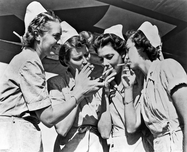 Black and white photo of four US Army nurses sharing a light for their cigarettes.