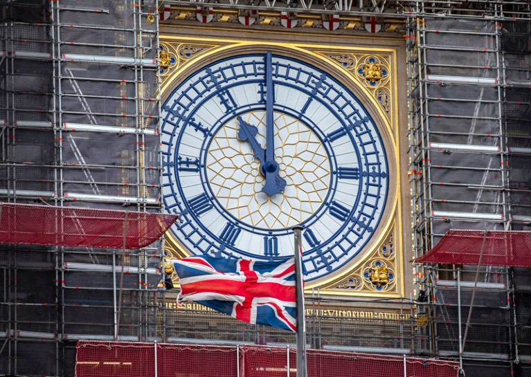 A Union Jack flag flying in front of the clock face of Elizabeth Tower showing 11 o'clock