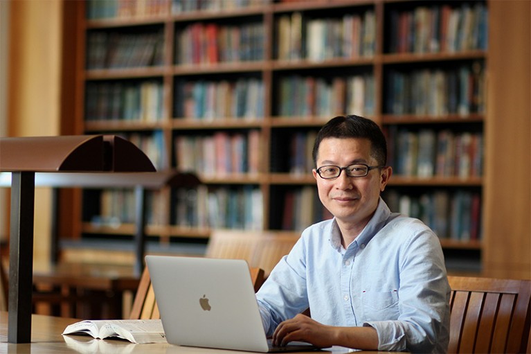 Xiaoming Zhou sits with his laptop at a desk in a library