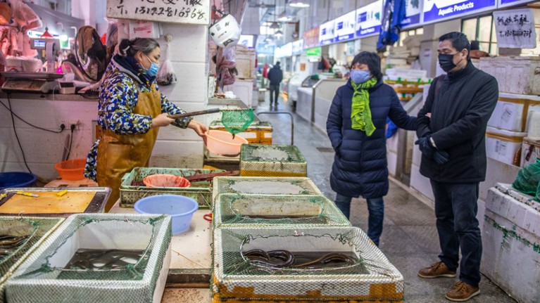 Woman store vendor wearing a mask shows living eel to couple wearing masks at seafood market.
