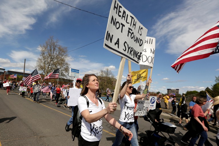 A demonstrator taking part in a protest march holds a sign reading "Health is not found in a syringe"