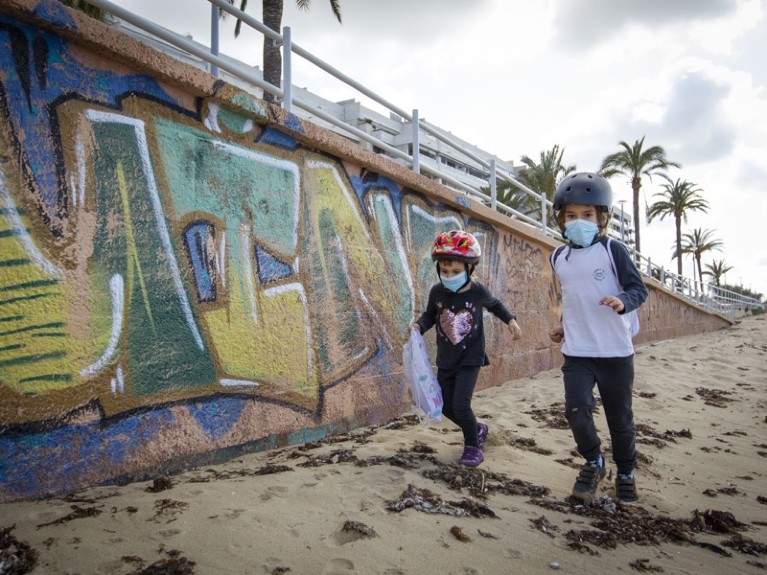 Two children wearing face masks play on Portixol Beach in Palma de Mallorca, on April 26, 2020 during a national lockdown.