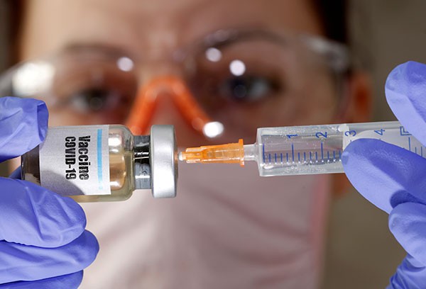 A woman holds a small bottle labeled with a "Vaccine COVID-19" sticker and a medical syringe.