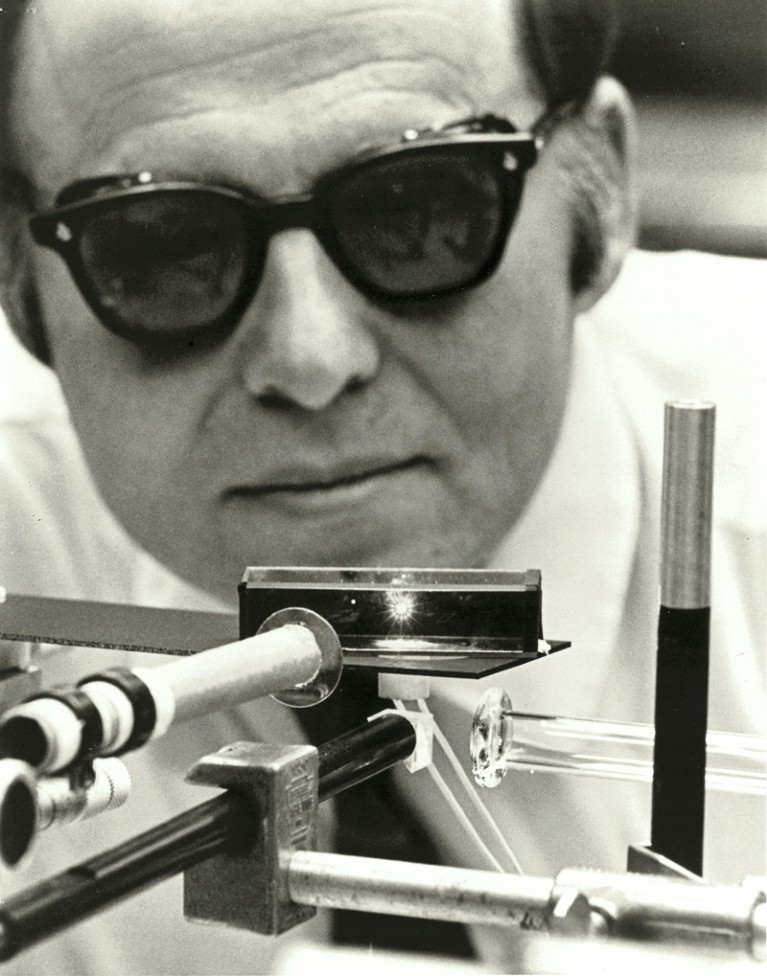 Black and white photo of Arthur Ashkin wearing dark goggles looking at laser equipment in the lab in 1971