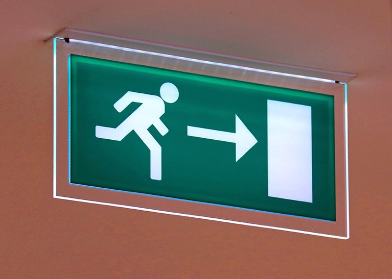 A green exit sign showing a stick figure of a person running towards a door directed by an arrow symbol