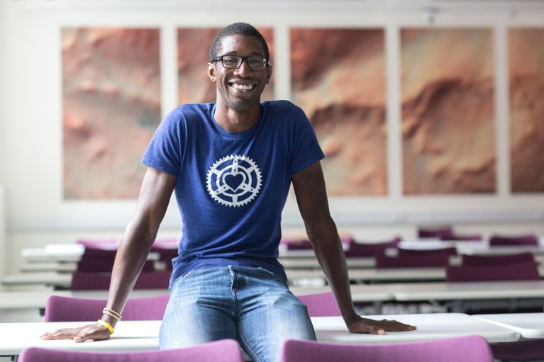 Christopher Jackson posing for a portrait sitting on a desk in a class room