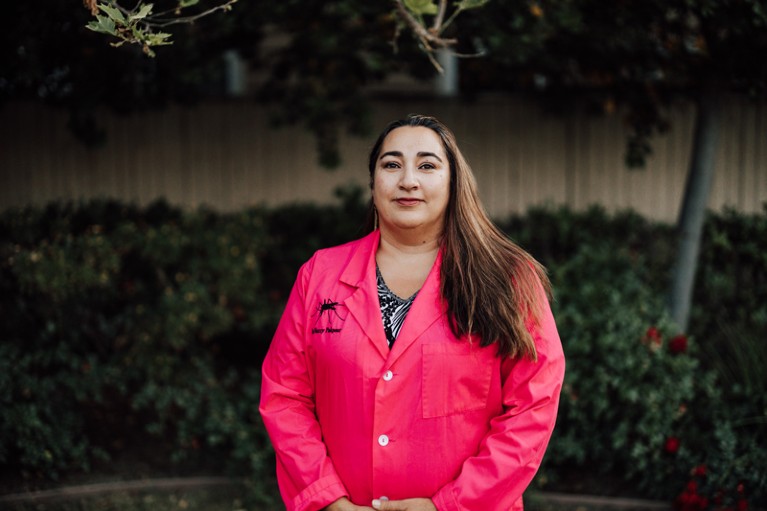 Nazzy Pakpour poses outside for a portrait wearing a bright pink lab coat