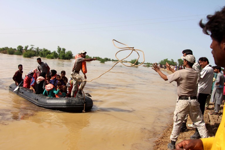 A navy soldier casts a rope from a small boat containing people being rescued from a flooded area in Pakistan