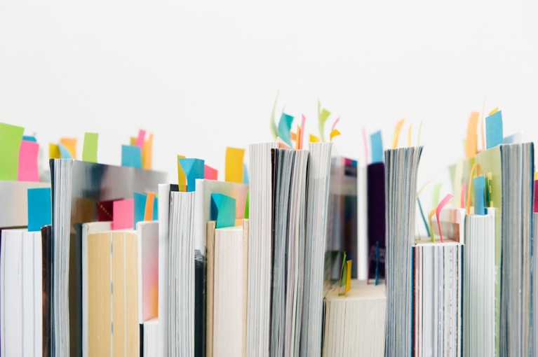 A row of books standing upright with coloured sticky notes marking pages