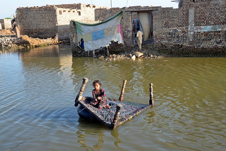 A girl sits on a cot while pulling a rope to cross a flooded street at Sohbatpur, Jaffarabad district, Balochistan, Pakistan.