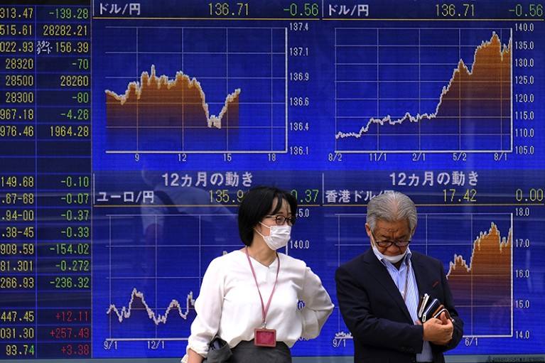 Two people stand in front of a stock prices board in Tokyo
