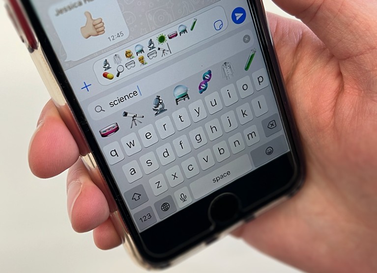 Close-up of a hand holding a phone showing science emojis.