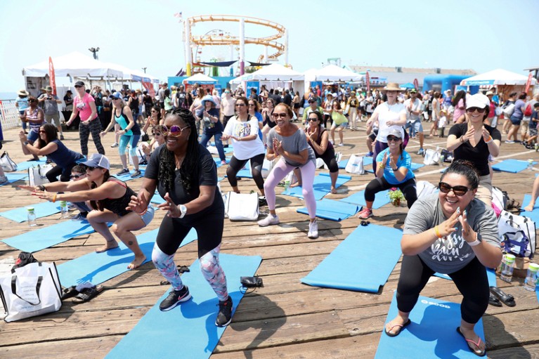 A group of people standing on blue yoga mats smile as they participate in an exercise class