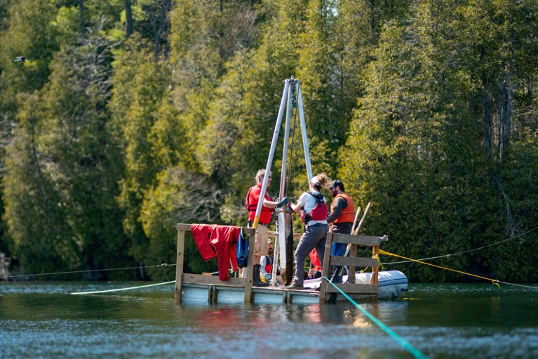 Researchers stand on a raft on the surface of Crawford Lake and pull up sediment core samples