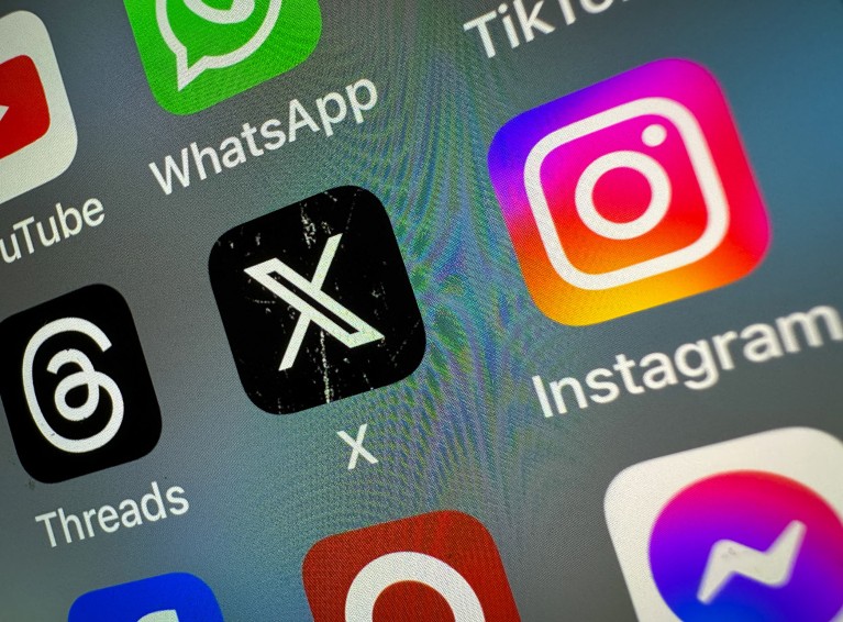 The logo of the social networking site 'X' (formerly known as Twitter) is displayed centrally on a smartphone screen alongside that of Threads (L) and Instagram (R).