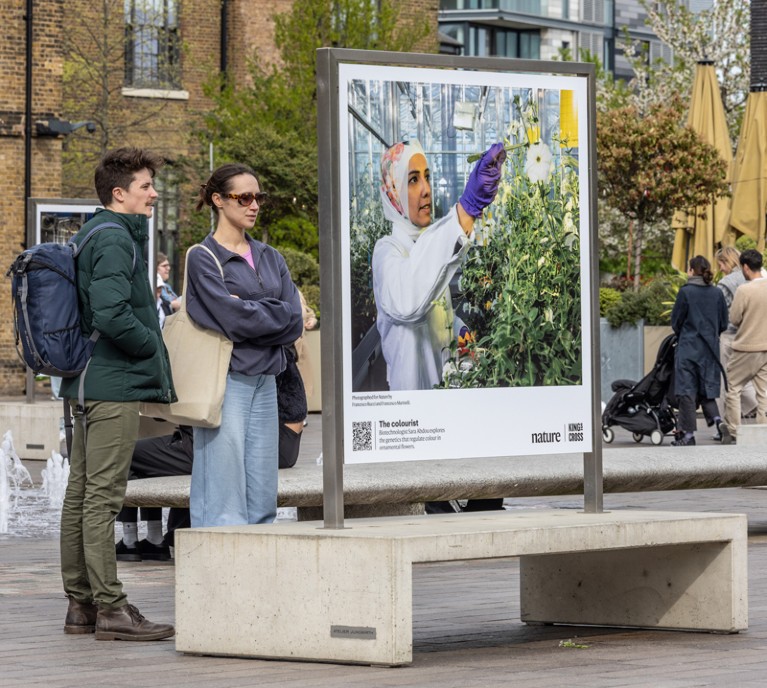 Memers of the public look at a photo in an outdoor exhibition of portraits of scientists