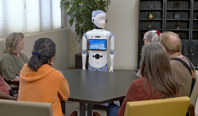 Five people sit around a table, facing a humanoid robot.