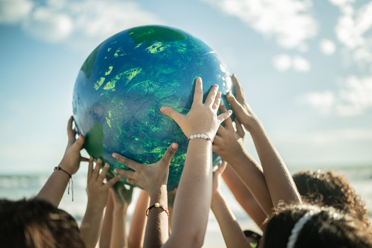 Close-up of a group of children holding a model planet Earth at the beach.