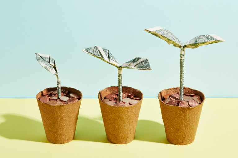 A row of three origami dollar seedlings growing in flower pots full of coins