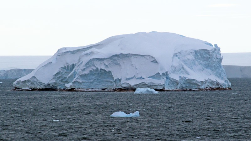 A thin strip of rocks in the sea, covered with a large ice cap.
