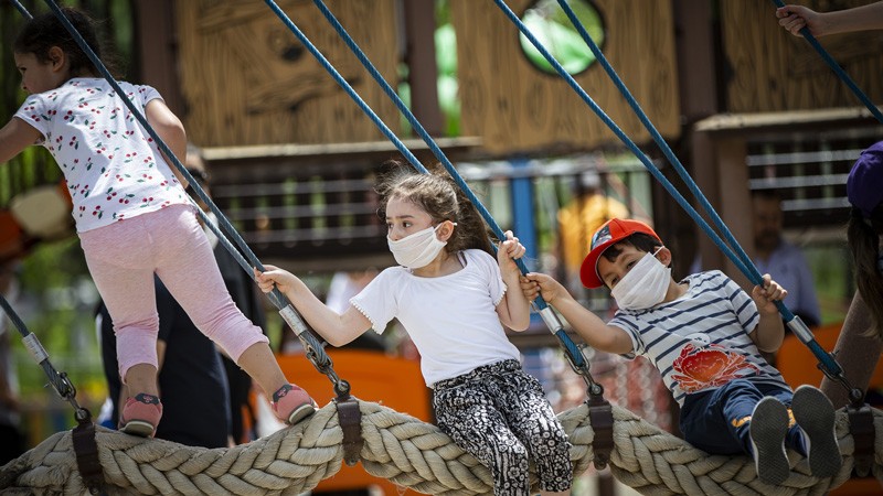 Kids wearing protective masks swing on a playground after children under 14 years across Turkey.