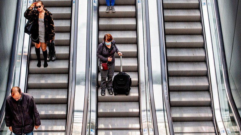 Three escalators, with people on two of them. One of the women wears a face mask.