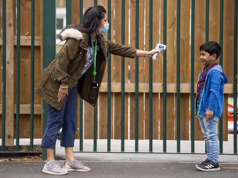 A child has his temperature checked by a teacher before entering Earlham Primary School, UK.