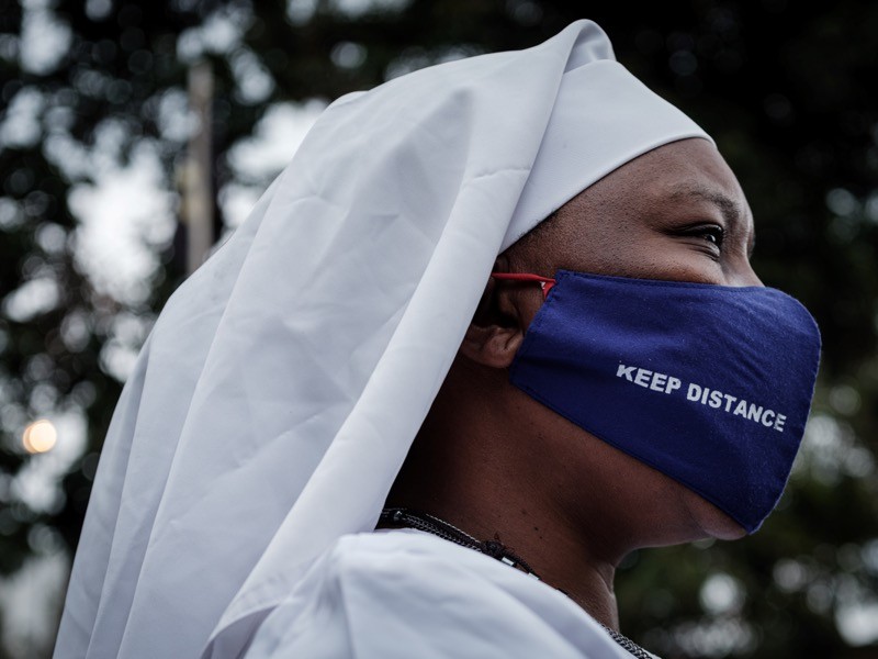 A worshipper of Legio Maria wears a protective face mask with the lettering 'Keep distance', Kenya.