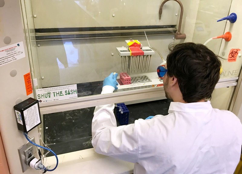 A researchers works at a fume hood installed with the MASH device