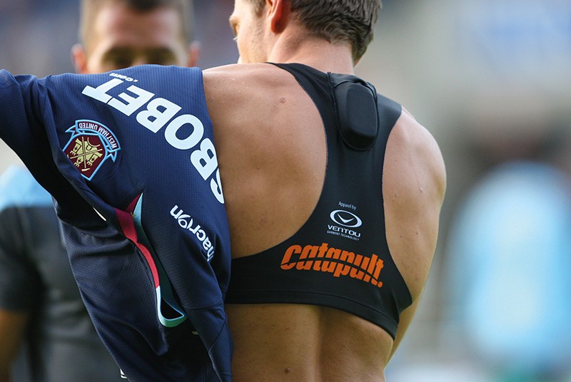 A male football player puts on a jersey over a vest containing a GPS sensor