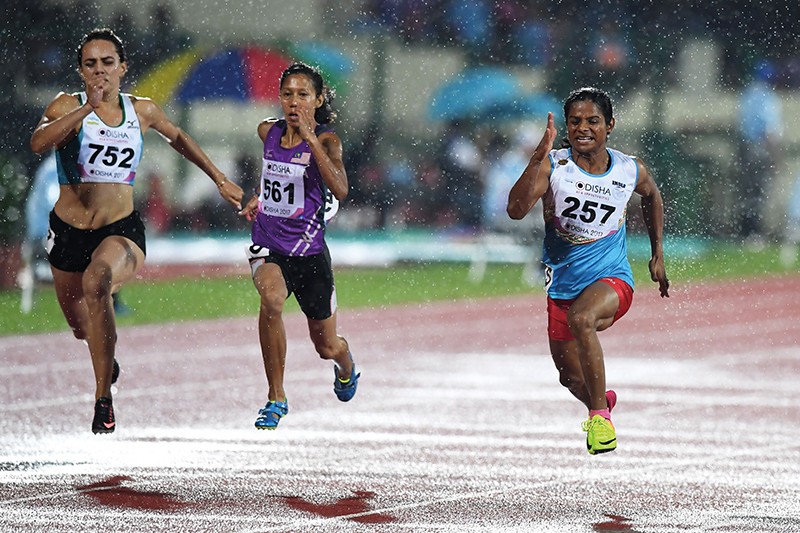 Three athletes sprint in the rain on an athletics track