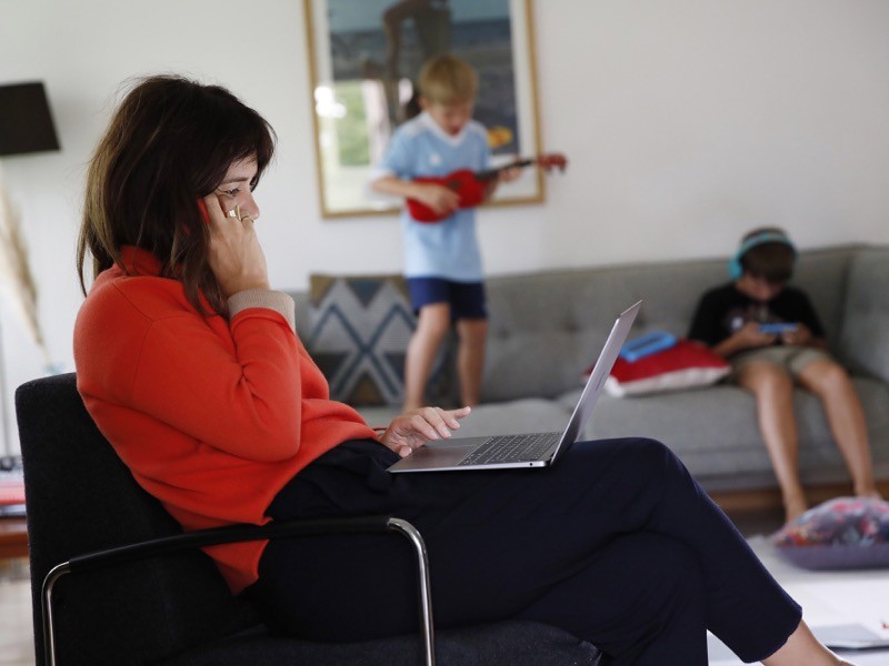 A woman works at a laptop computer in a lounge as children play beyond.