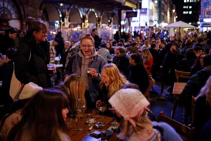 large numbers of people in coats sitting at outside tables, drinking.
